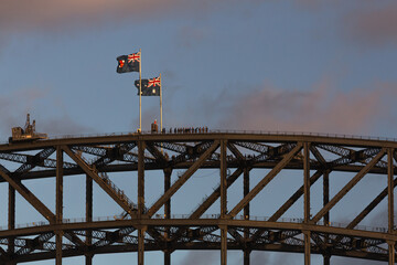 A group of sightseers stand atop the Sydney Harbour Bridge, at the flag poles with the Australian and New South Wales flags, late afternoon. Copy space.