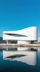Obraz premium Modern white building with a curved design reflected in calm water under a clear blue sky