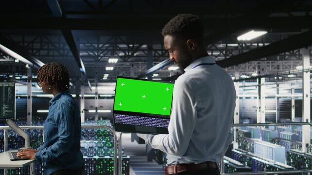 Technicians on data center industrial platform analyzing performance outputs on green screen laptop. Server hub engineering team finetuning server rig configurations using mockup notebook, camera A
