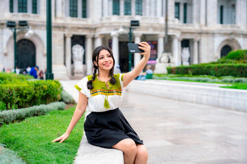 Happy young Latina with braided hair takes a selfie sitting on a garden bench near Palacio de...