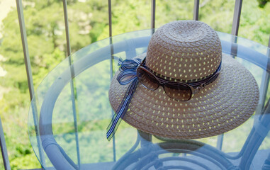 Summer straw hat and sunglasses close-up on a glass table on the balcony