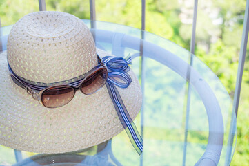 Summer straw hat and sunglasses close-up on a glass table on the balcony