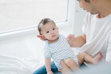 Asian devoted young father lovingly holds his three-month-old baby in a warm, inviting room. Their close bond radiates affection, peaceful atmosphere of comfort, safety, and unconditional love.