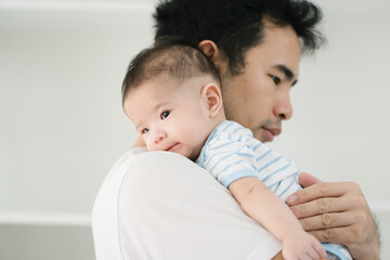 Asian devoted young father lovingly holds his three-month-old baby in a warm, inviting room. Their close bond radiates affection, peaceful atmosphere of comfort, safety, and unconditional love.