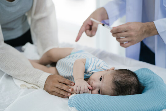 Fototapeta Asian loving mother comforts her three-month-old, as a male doctor administers essential childhood vaccinations, ensuring the baby's healthy future in a calm, professional setting.