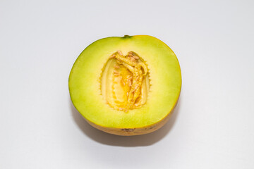 A halved melon, revealing bright green flesh and a central cavity filled with seeds and pulp, on a white background.