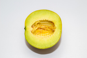 A halved melon, revealing bright green flesh and a central cavity filled with seeds and pulp, on a white background.
