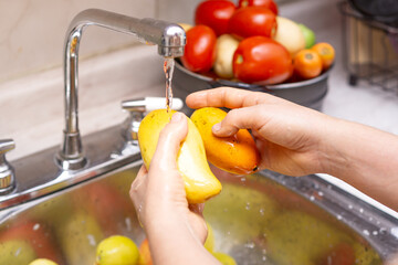 Woman washing organic mango, food disinfection concept