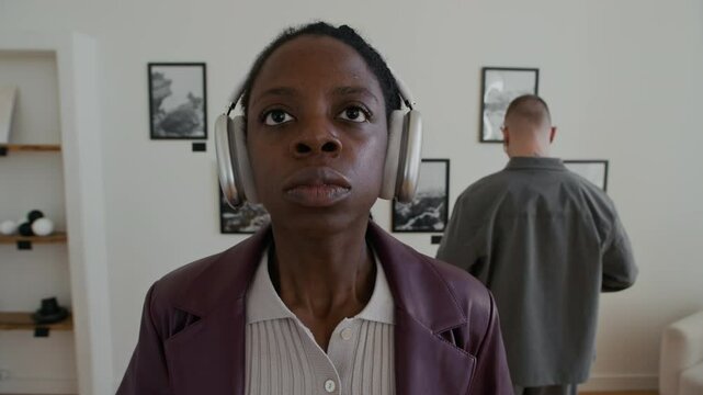 Front view closeup shot of young African American woman putting on headphones with audio guide description while looking at art in museum