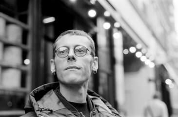 Young man wearing glasses posing in urban setting with analog film grain
