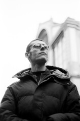 Pensive man wearing glasses and winter coat looking up in urban setting, analog style portrait