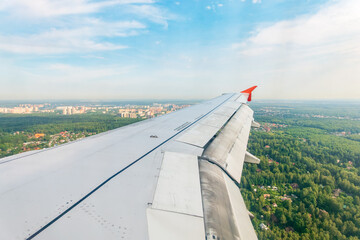 View of airplane wing, blue skies and green land during landing. Airplane window view.