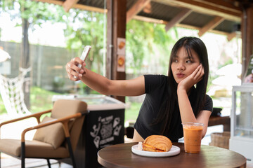 young woman having breakfast in cafe and having video call with friend