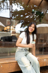 young woman sitting on a bench in the city coffee shop while smiling