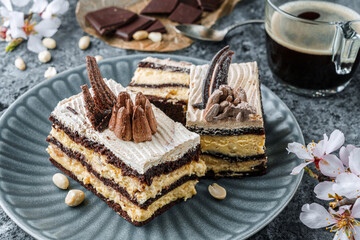 Chocolate biscuit layer cake with nuts and cream on the plate on grey background with flowers. Sweets, dessert and pastry, homemade cakes, close up, selective focus