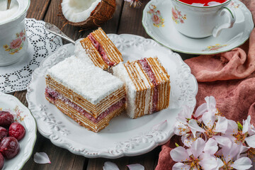 Homemade Sour cream cake with cherries and coconut on plate on wooden background with flowers. Sweets, dessert and pastry, top view