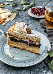 Piece of biscuit cake with cherry and cream on the plate on grey background with flowers. Sweets, dessert and pastry, homemade cakes, close up, selective focus