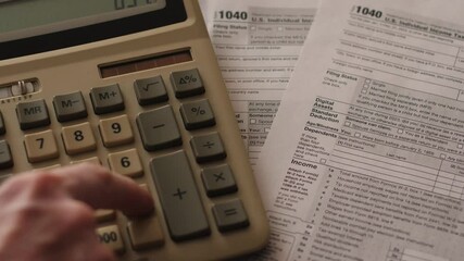 Close-up of tax calculation and payment, filling out tax form 1040, with a calculator computing taxes alongside a sheet of the 1040 declaration - Powered by Adobe