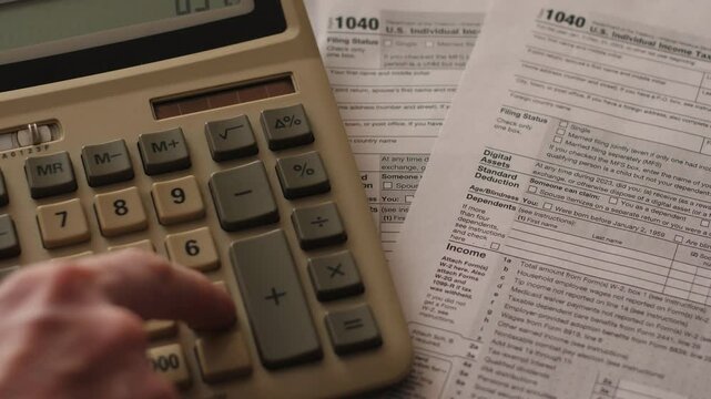 Close-up of tax calculation and payment, filling out tax form 1040, with a calculator computing taxes alongside a sheet of the 1040 declaration