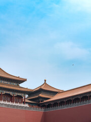 Traditional rooftops of the Forbidden City under clear blue sky with a bird flying overhead,...