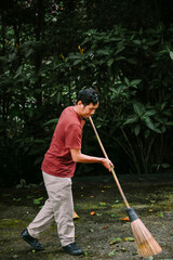 Man sweeps leaves with a traditional broom in a lush garden scene