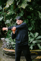 Young man stretching arm muscles outdoors in a tropical garden