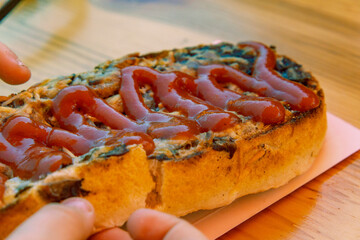 traditional Polish street food called zapiekanka – an open-faced baguette with mushrooms, cheese, and ketchup. Served on a piece of paper and held in hands.