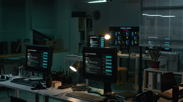 Full no people shot of computer screens on desks in dark scam call center at nighttime, with personal profiles on victims, chat messages, bank transfers and stolen cash counters