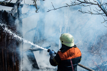Firefighter put out a fire. Brave firefighter battling house fire blaze. Firemen in uniform in...
