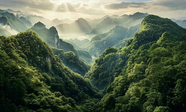 Aerial view of a lush green mountain range with dramatic peaks under vibrant sunlight and scattered clouds in a clear blue sky.