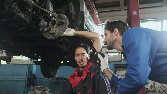 Two male mechanics cooperate, Latin and Asian workers fixing automotive wheels and maintaining car suspensions in garage station, and technician engineering service jobs in vehicle transport industry.