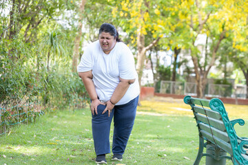 Overweight indian woman suffering from knee pain while walking in summer park .Plus size lady have...