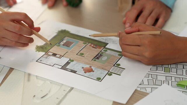 Professional engineer team discussion about house design on meeting table with architectural equipment and building blueprint scatter around at modern office. Focus on hand. Closeup. Delineation.