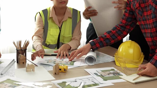 Smart architect and safety engineer discussion about building blueprint on table with architectural document, measurement tools and wooden block scatter around at modern office. Closeup. Delineation.