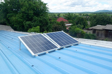 Two large solar panels are installed on a blue metal roof of a rural house using steel legs to support them.