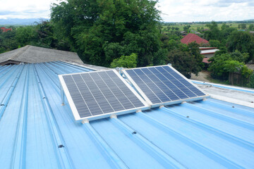 Two large solar panels are installed on a blue metal roof of a rural house using steel legs to support them.