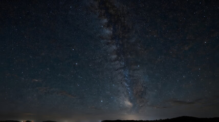 Majestic Milky Way Galaxy stretches across a dark night sky above a distant horizon, showcasing countless stars and celestial wonders.