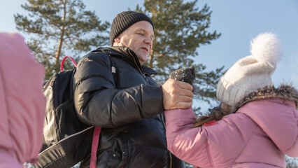 Grandfather walks with his granddaughters after school in the park in sunny winter day