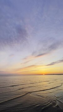 Sea waves rolling on sand beach in golden hour at sunset. Ocean ripples on grey ocean surface at sunrise. Colorful Sunset on seaside. Nature wallpaper. Peaceful natural scene. vertical 9x16 4k.