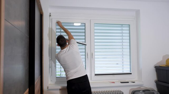 Static shot of a man carefully mounting a pleated window shade during a home DIY project in a bedroom, aligning the frame and pressing it into place for a snug fit.