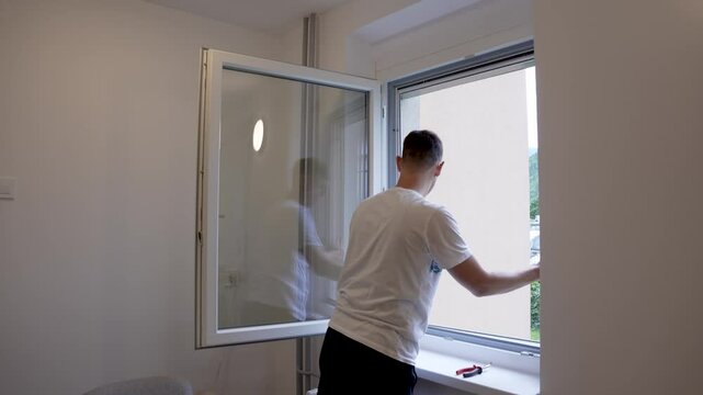 Static timelapse shot of a man installing a fixed mosquito net on a window frame as part of a DIY home improvement project, showing step-by-step progress in fast motion.