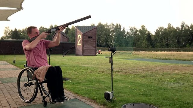 young man with double-barreled shotgun in wheelchair practicing clay pigeon shooting