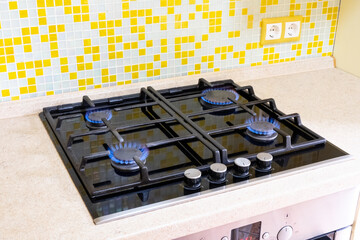 Close-up of a four-burner gas stove in a home kitchen. Bright blue flames
