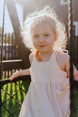 A joyful 3-year-old girl plays in the backyard, swinging happily on a swing. Surrounded by greenery and sunshine, she smiles brightly, enjoying a carefree moment of childhood fun and freedom