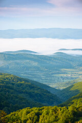 mountainous countryside landscape with fog in the distant valley. mist rolling among hills in morning light. stunning view of carpathians in summer. clouds on the blue sky. amazing dale