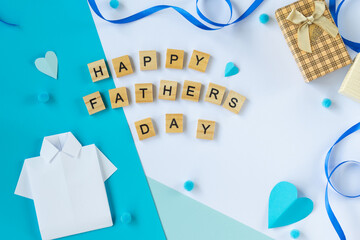 Greeting composition with Fathers Day wooden letters paper shirt tie hearts gift box blue background top view flat lay layout handmade dad celebration concept social content