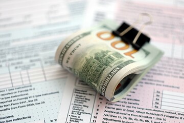 Big amount of United States USD dollar bills banknotes on table with 1040 tax return form
