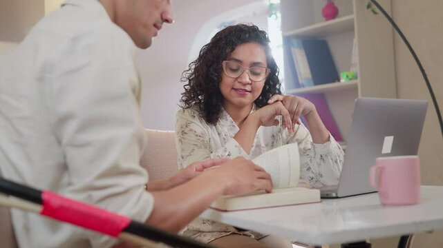 Two young, attractive, smiling university colleagues or friends interacting and busy discussing and reading a book in a cafe or coworking space. Friendship, relationship, communication concept.