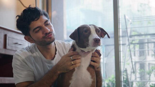 A young Indian Asian affectionate male or a man hugging and embracing his adopted, cute female stray pet dog in an interior house or apartment. Human animal friendship, bonding, companionship concept