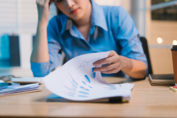 Working late into the night, Asian woman appears stressed and overwhelmed at her desk, rubbing her...
